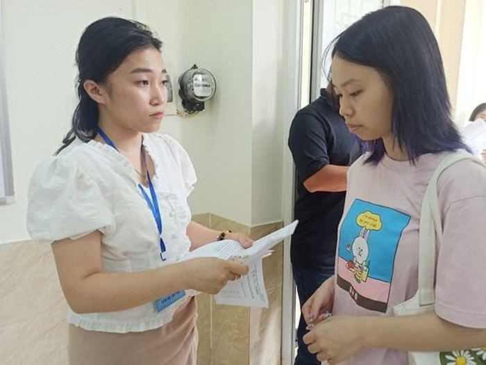 Cán bộ coi thi kiểm tra thông tin của thí sinh trước khi vào phòng thi. (Ảnh: Phạm Mai/Vietnam+)